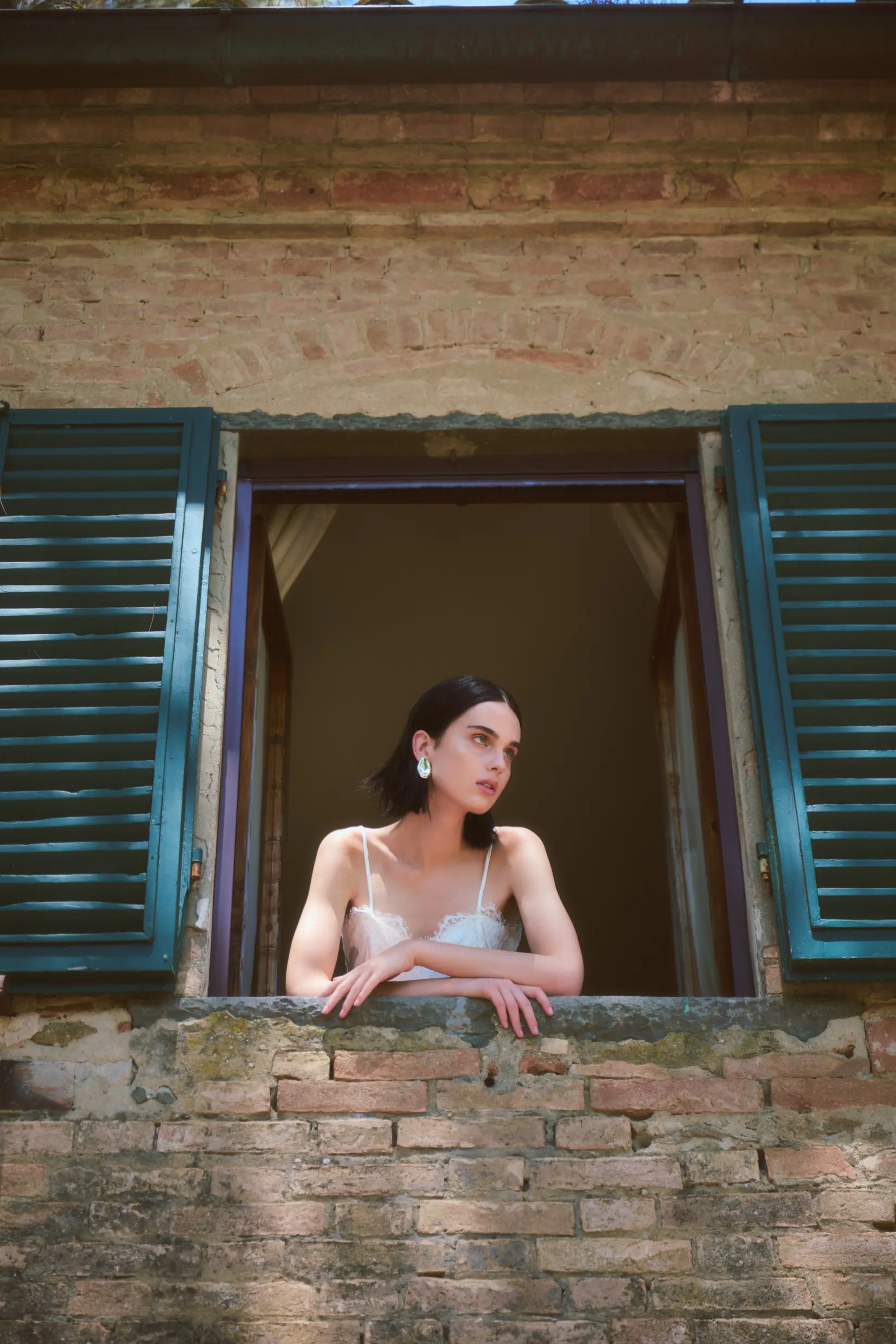 Full-length view of the woman in sculptural tailoring before a weathered villa façade.