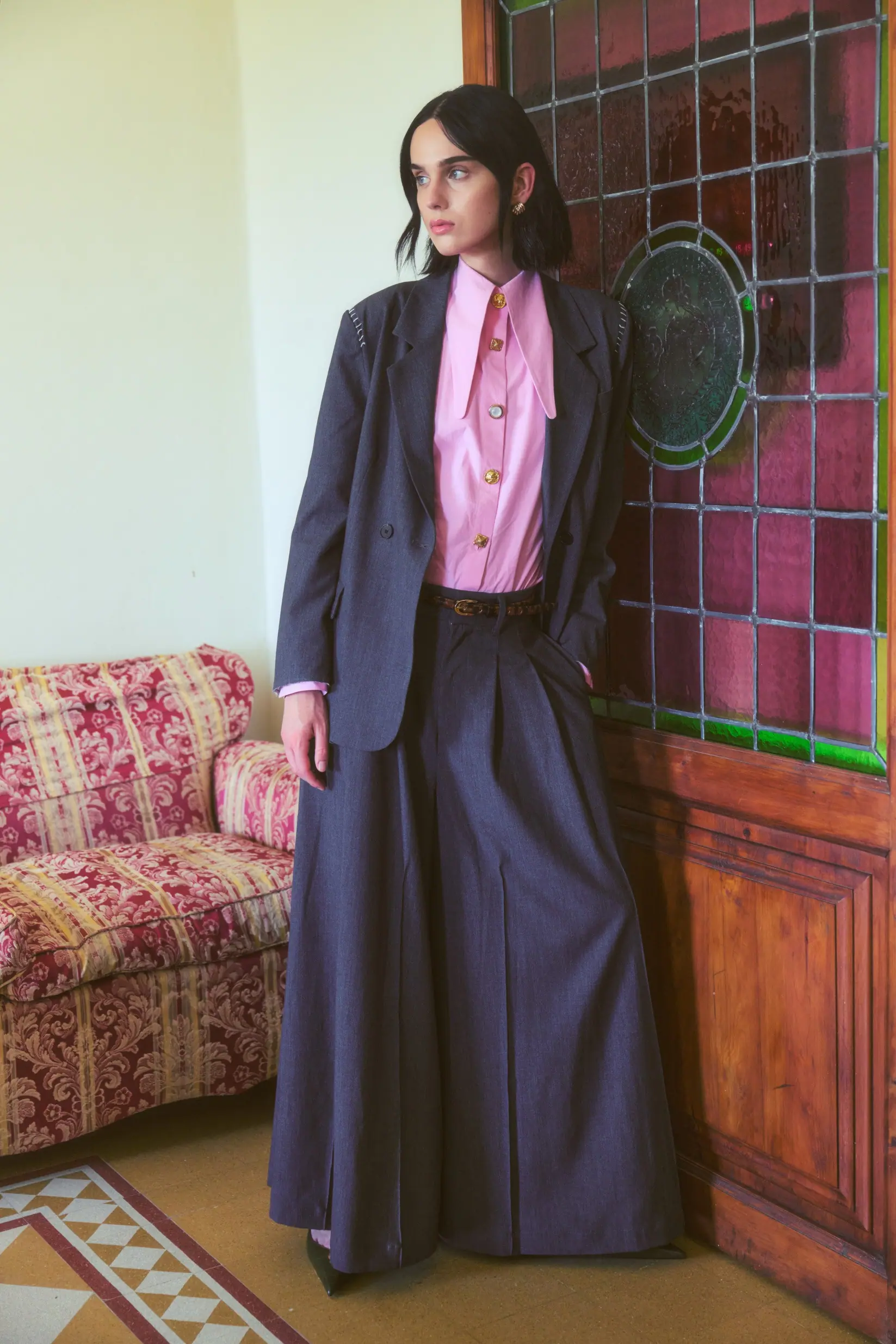 A woman in lightweight tailoring crossing a sunlit terrace.